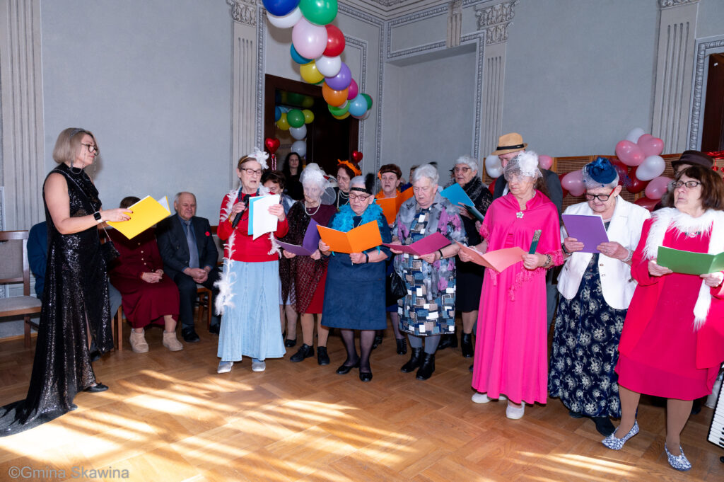 Grupa seniorów występuje przed publicznością i śpiewa 