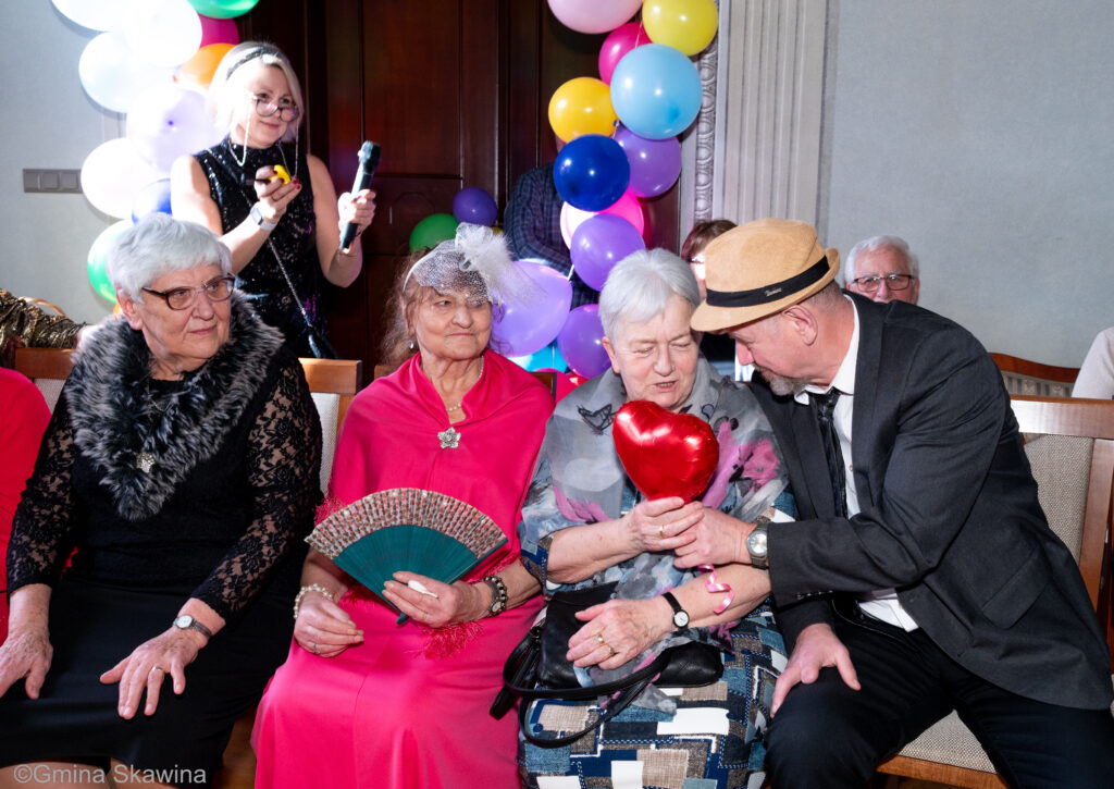 Senior podaje seniorce czerwony balon w kształcie serca