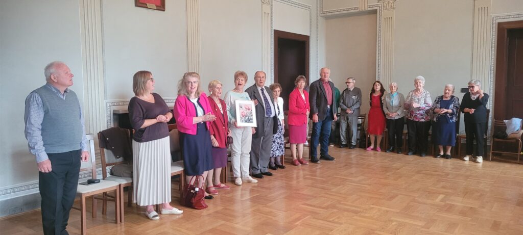 Seniorzy stoją w półkole i śpiewają