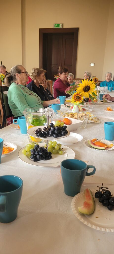 Stół z owocami wokół którego siedzą seniorzy