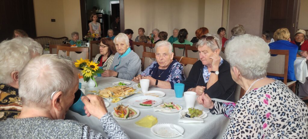 Seniorzy siedzą przy stoliku i jedzą przekąski