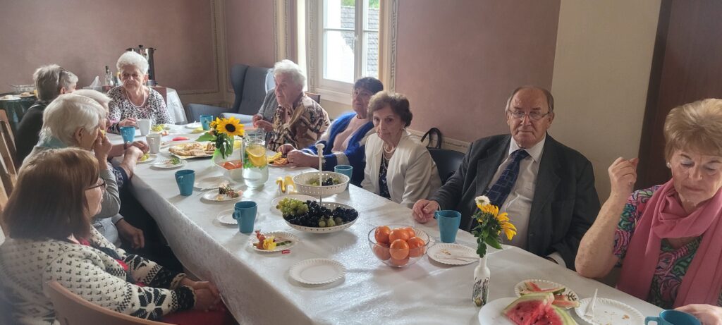Seniorzy siedzą wokół stolika na którym są owoce