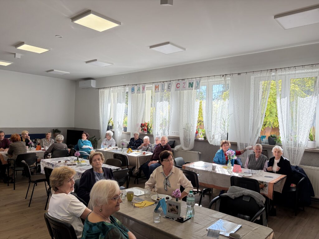 Seniorzy siedzą przy ponumerowanych stolikach
