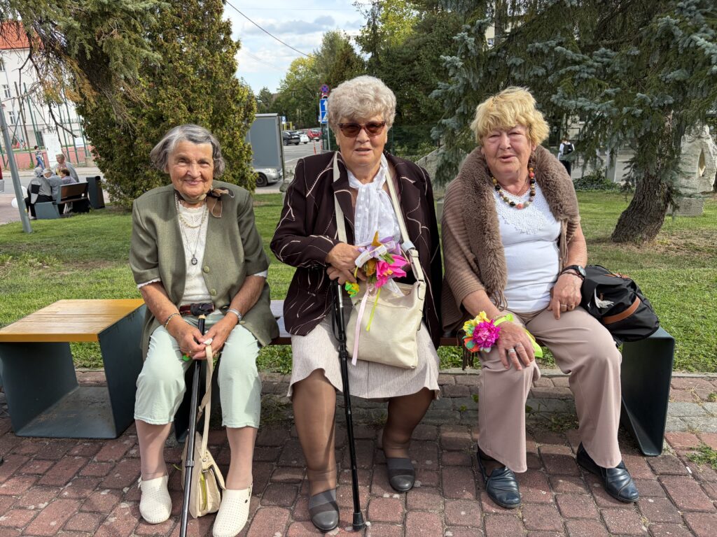 Trzy uśmiechnięte seniorki siedzą na ławeczce