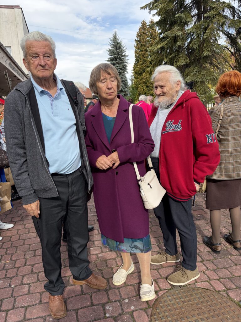 Trzech seniorów kobieta w środku po bokach mężczyźni stoją i pozują do zdjęcia